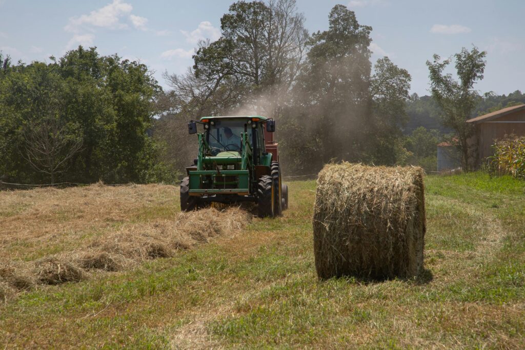 pexels-photo-2737098-2737098 Green tractor in a North Carolina field with hay bales being harvested on a sunny day.